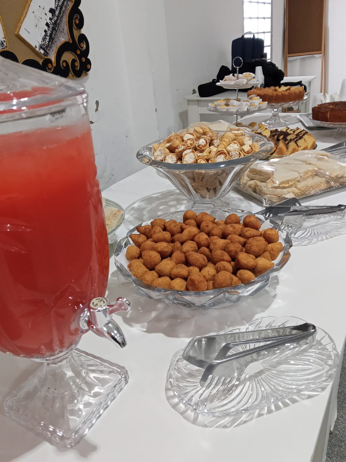 Suqueira de vidro ao lado de mesa com salgados e bolos servidos