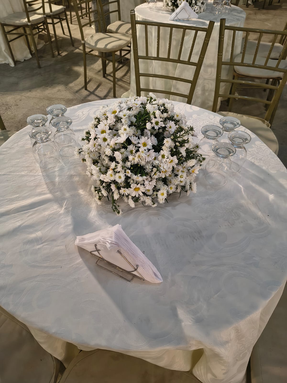 Mesa redonda posta com toalha branca, arranjo de flores e taças de vidro