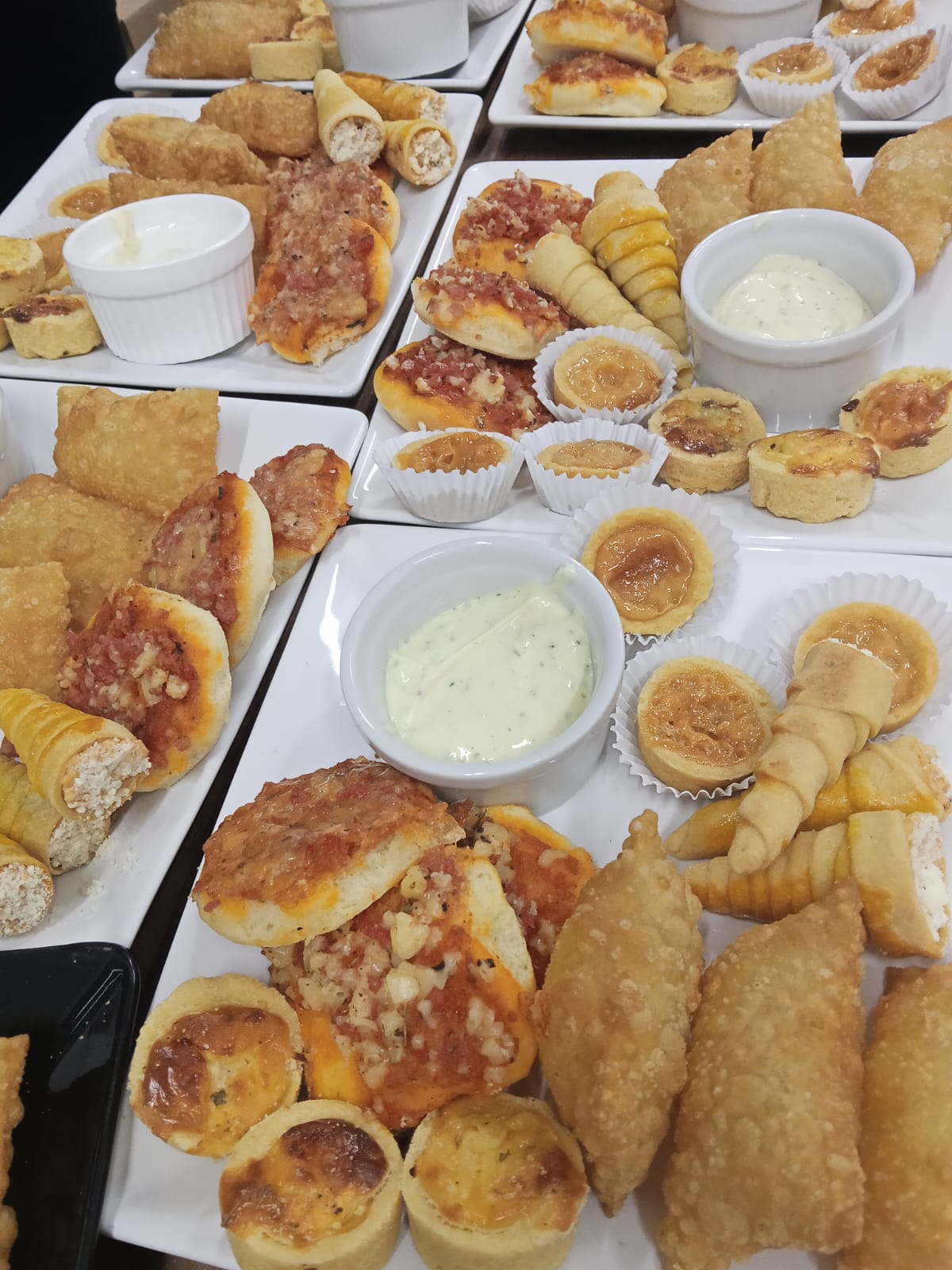 Travessas com salgados variados, empadinhas e molhos servidos em evento